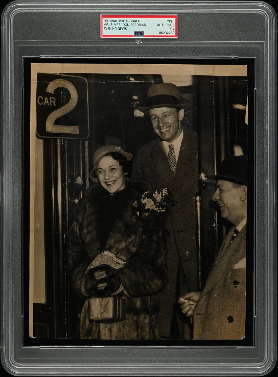 PSA Type I original photograph of Sir Donald Bradman with his wife (1934 Evening News) — front shows the couple in a candid moment; reverse shows copyright stamp, 18 Dec 1934 date, and newsroom crop notes, PSA Authentic.